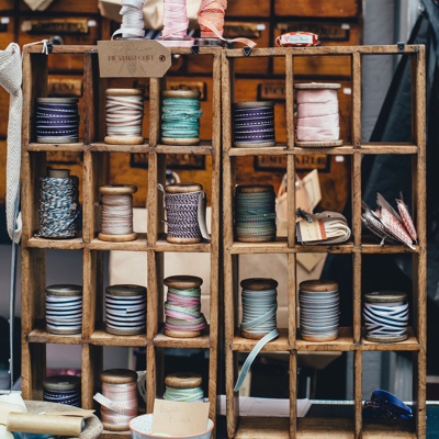 A small wooden shelf filled with spools of a variety of ribbons and string.